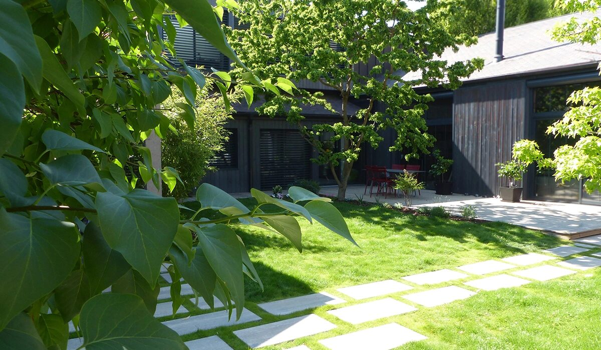 Aménagement paysager terminé par TMD Paysage : pelouse engazonnée et allée en pas japonais devant une terrasse bois